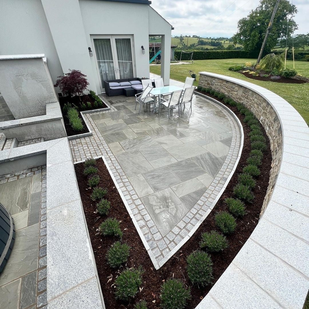 Outdoor patio area with a curved stone path leading to a house. Paving is Grey Sandstone Patio Packs. 