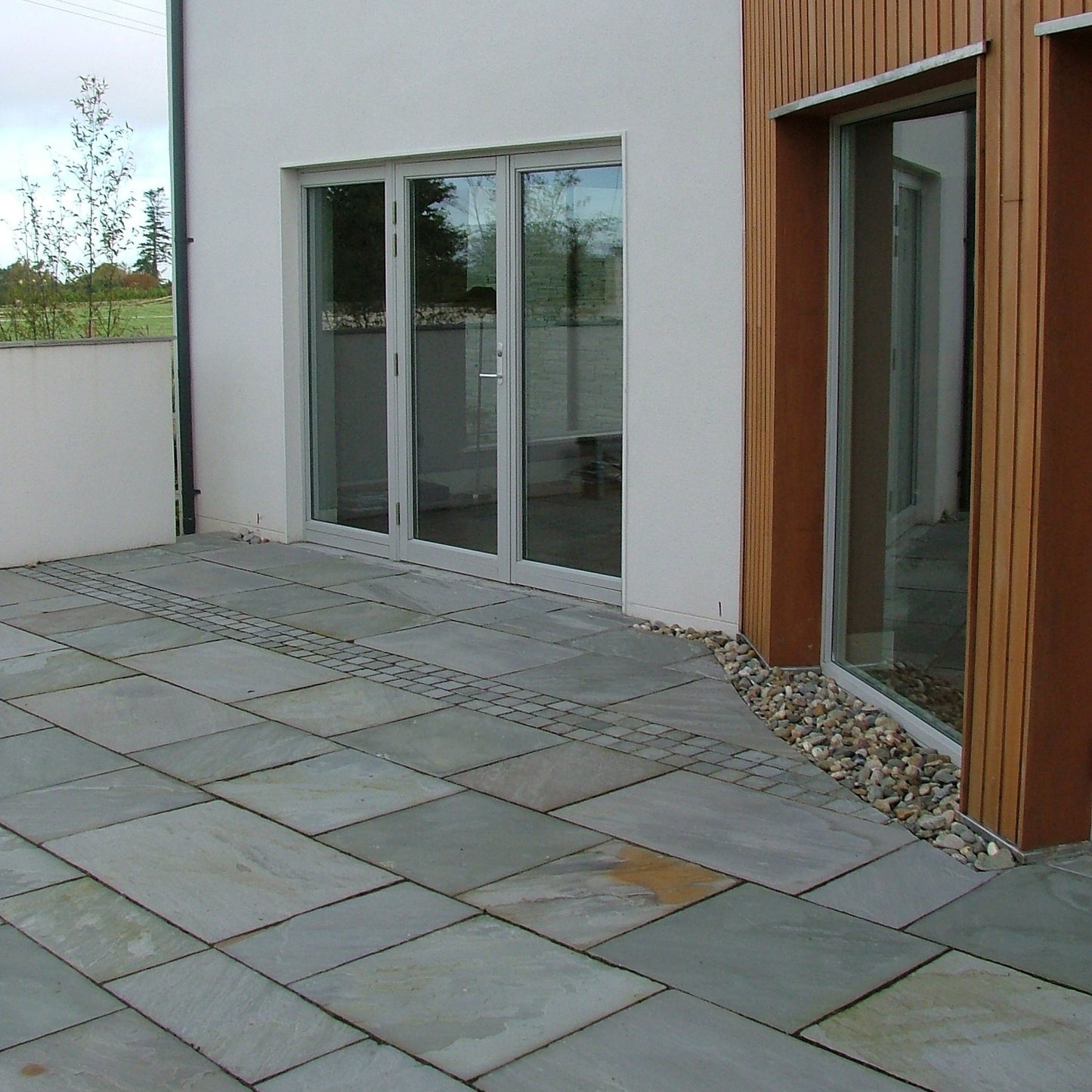 Modern house with wooden cladding. Patio completed using Grey Sandstone Paving in mixed sizes. 