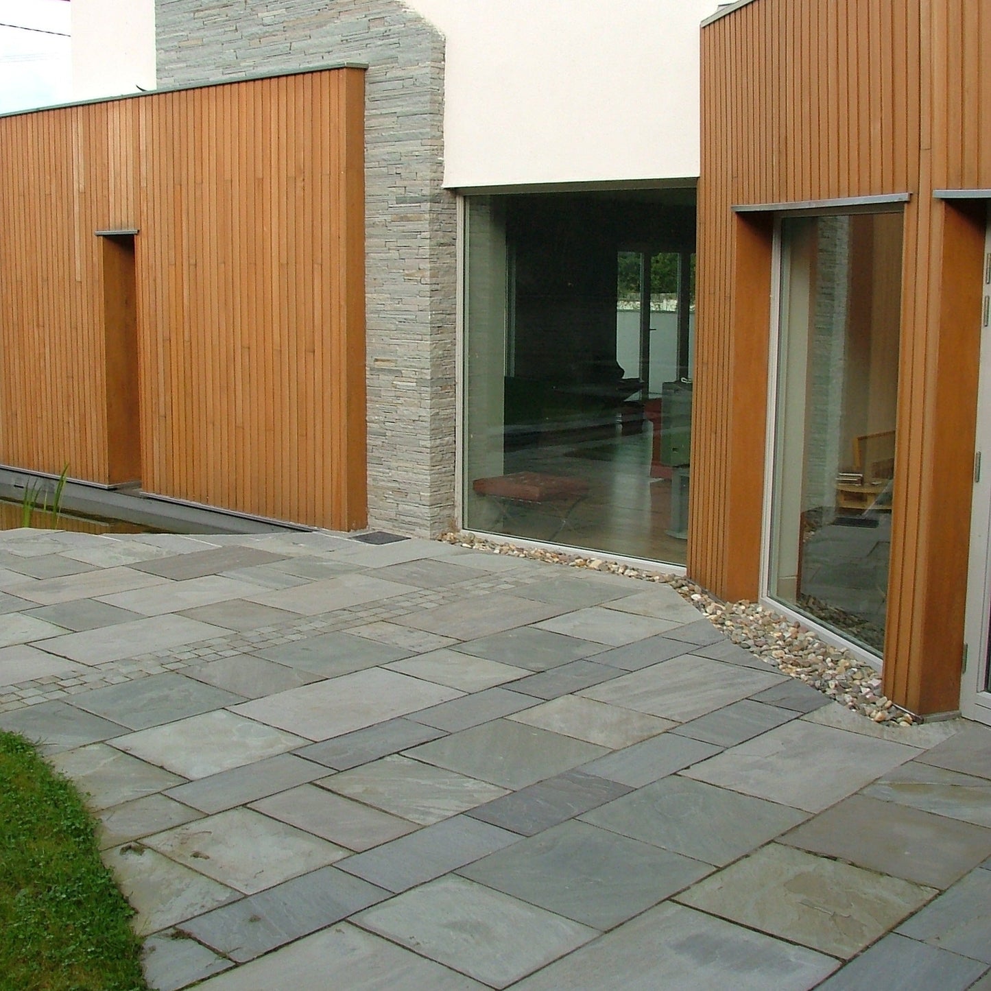 Modern house with Grey Sandstone Paving and wooden wall cladding. 