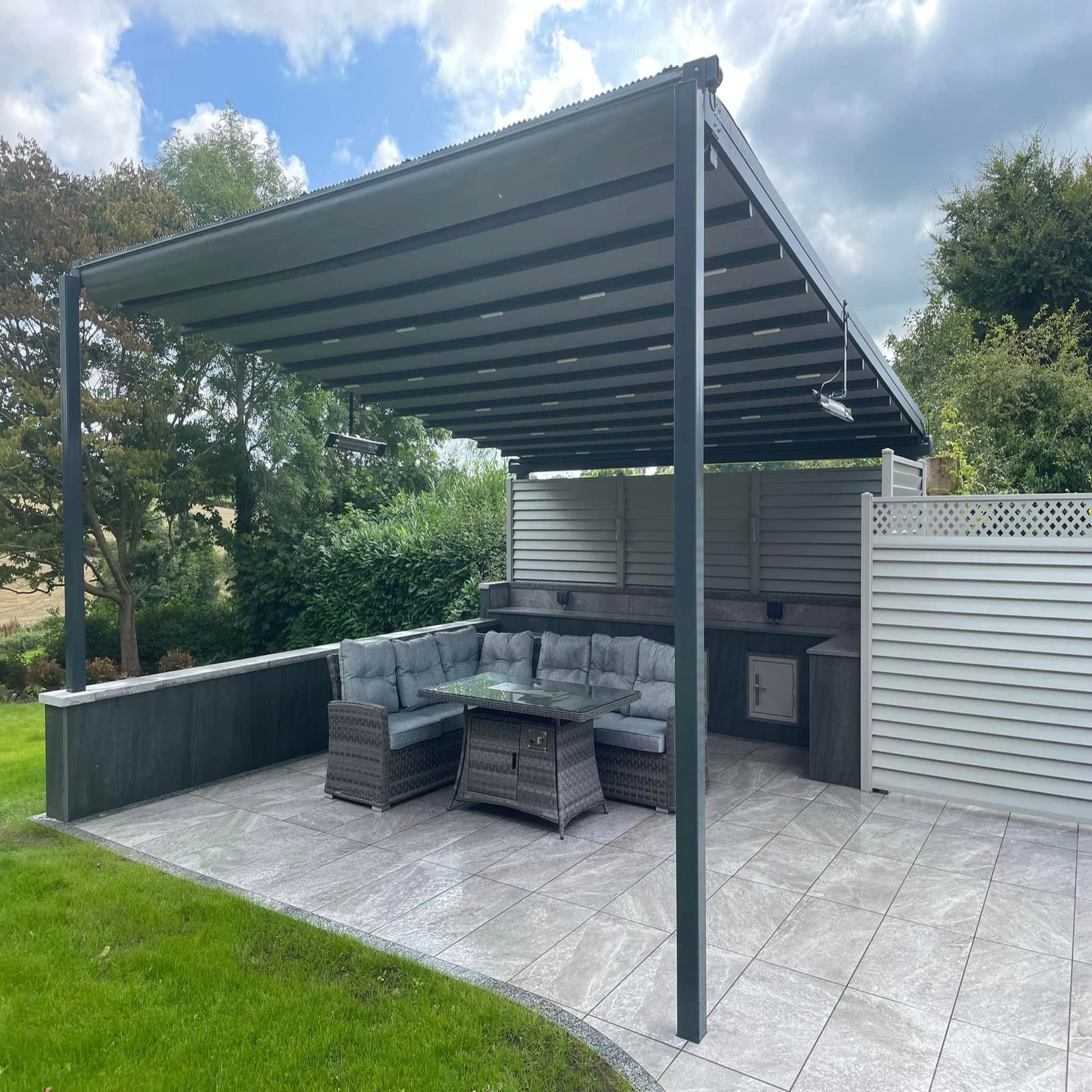 A patio area with Twice Qz Range porcelain paving tiles and outdoor furniture set under a grey pergola.
