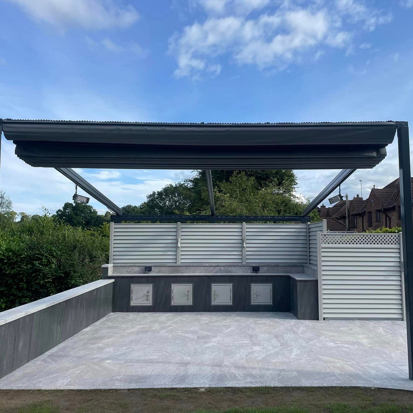 Patio area featuring Grey Twice Qz Range Porcelain Paving Tiles with Grey Pergola and BBQ counter with privacy fence. 