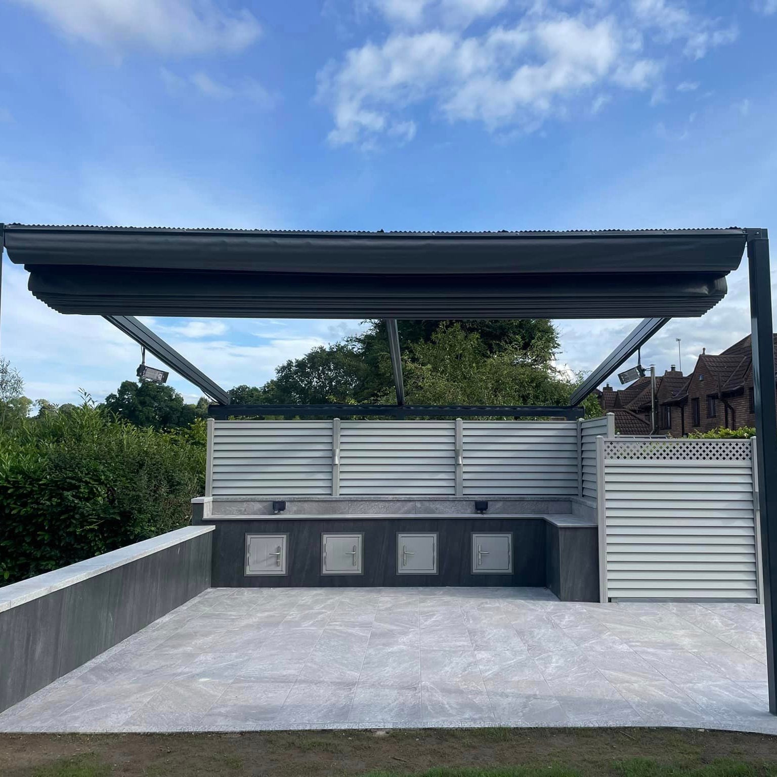 Patio area featuring Grey Twice Qz Range Porcelain Paving Tiles with Grey Pergola and BBQ counter with privacy fence. 