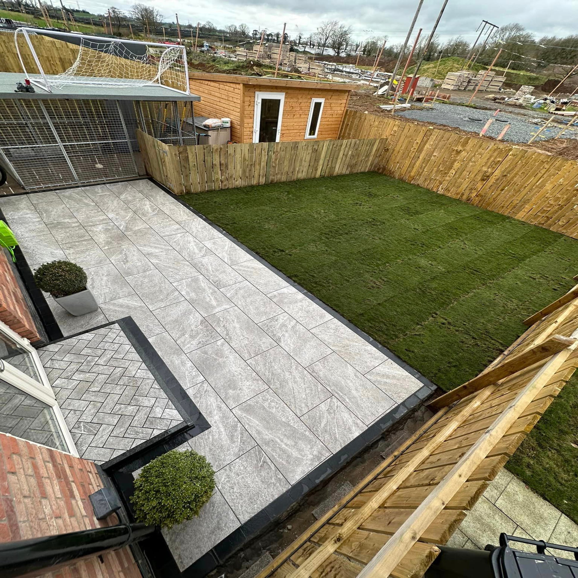 A residential landscaping project featuring grey twice qz porcelain paving with wooden fences. 
