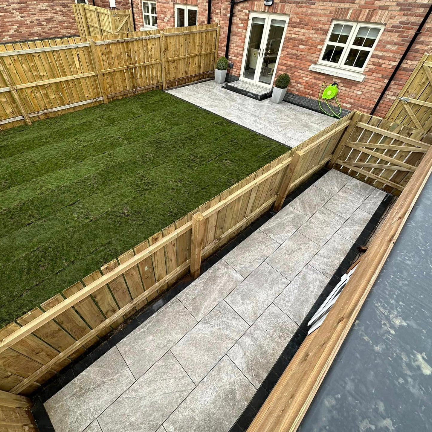 Small backyard featuring Grey Twice Qz Range Porcelain Paving Tiles and garden surrounded by wooden fencing. 