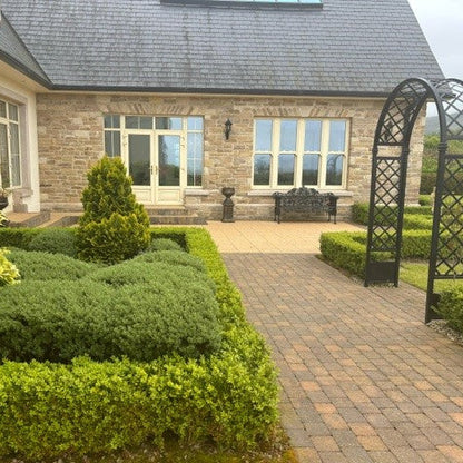 Neatly trimmed bushes in front of a house with a paved pathway and garden arch. Stone façade is Grit Sandstone.