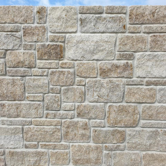 A close-up image of a constructed stone wall made from Grit Sandstone with a modular and tumbled finish, displaying a blend of golden brown and creamy beige tones.