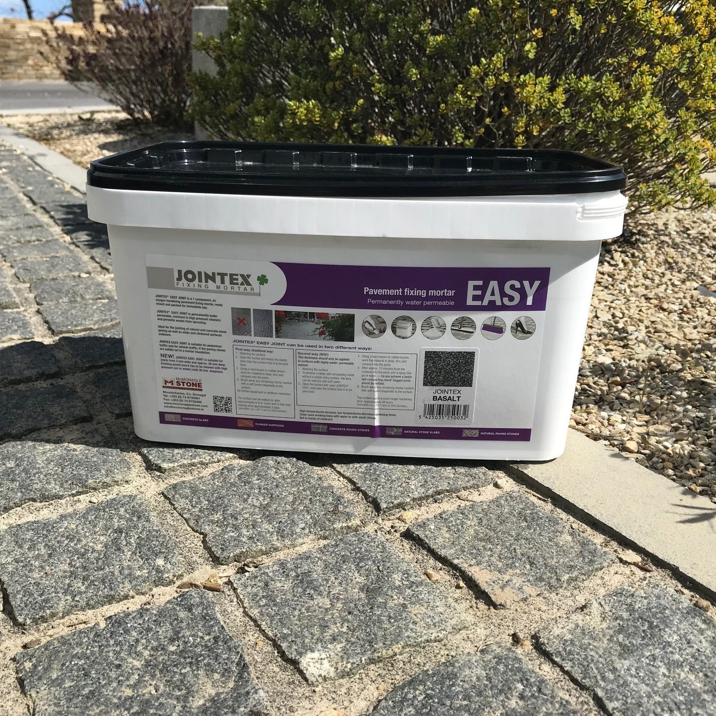 A 15kg tub of JOINTEX Easy Joint pavement mortar in Basalt color on dark cobble pavement. 