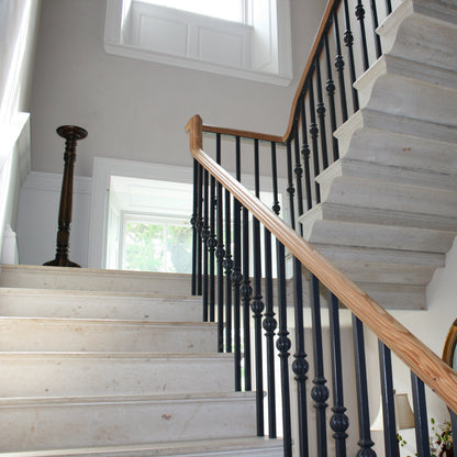 Bespoke Limestone Cantilevered Staircase with wooden handrail and black balusters in a well-lit room.