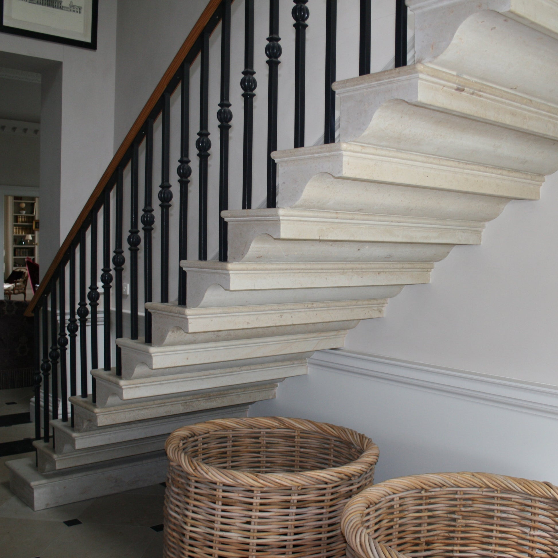 Bespoke limestone cantilevered staircase with black railings in a room with framed pictures on the wall.