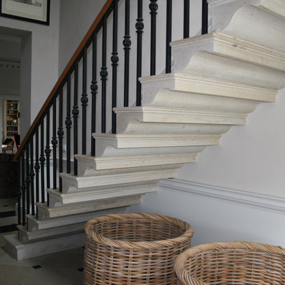 Bespoke limestone cantilevered staircase with black railings in a room with framed pictures on the wall.