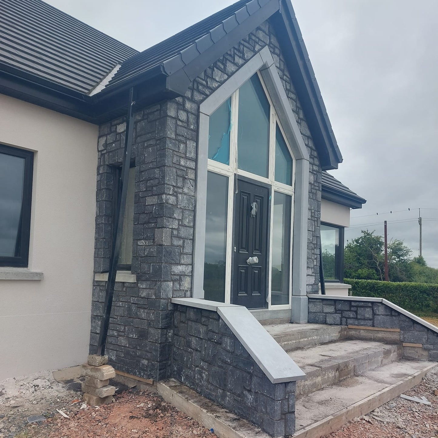 House exterior with stone facade and large windows under a cloudy sky. Features large blue limestone door surround.  