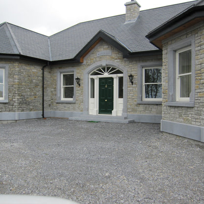 Stone house with a gravel driveway on a cloudy day. House features bespoke blue limestone door and window surrounds with a matching plinth and steps. 