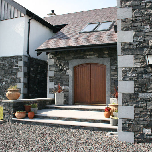 Stone house exterior with a wooden door and bespoke Blue Limestone Door Surround and Quoins. 