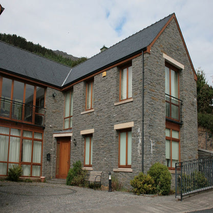 A two storey building constructed with Liscannor Slate, showing a gray stone finish with occasional brown variations, a window with a brown frame and gold granite lintels and sills. 