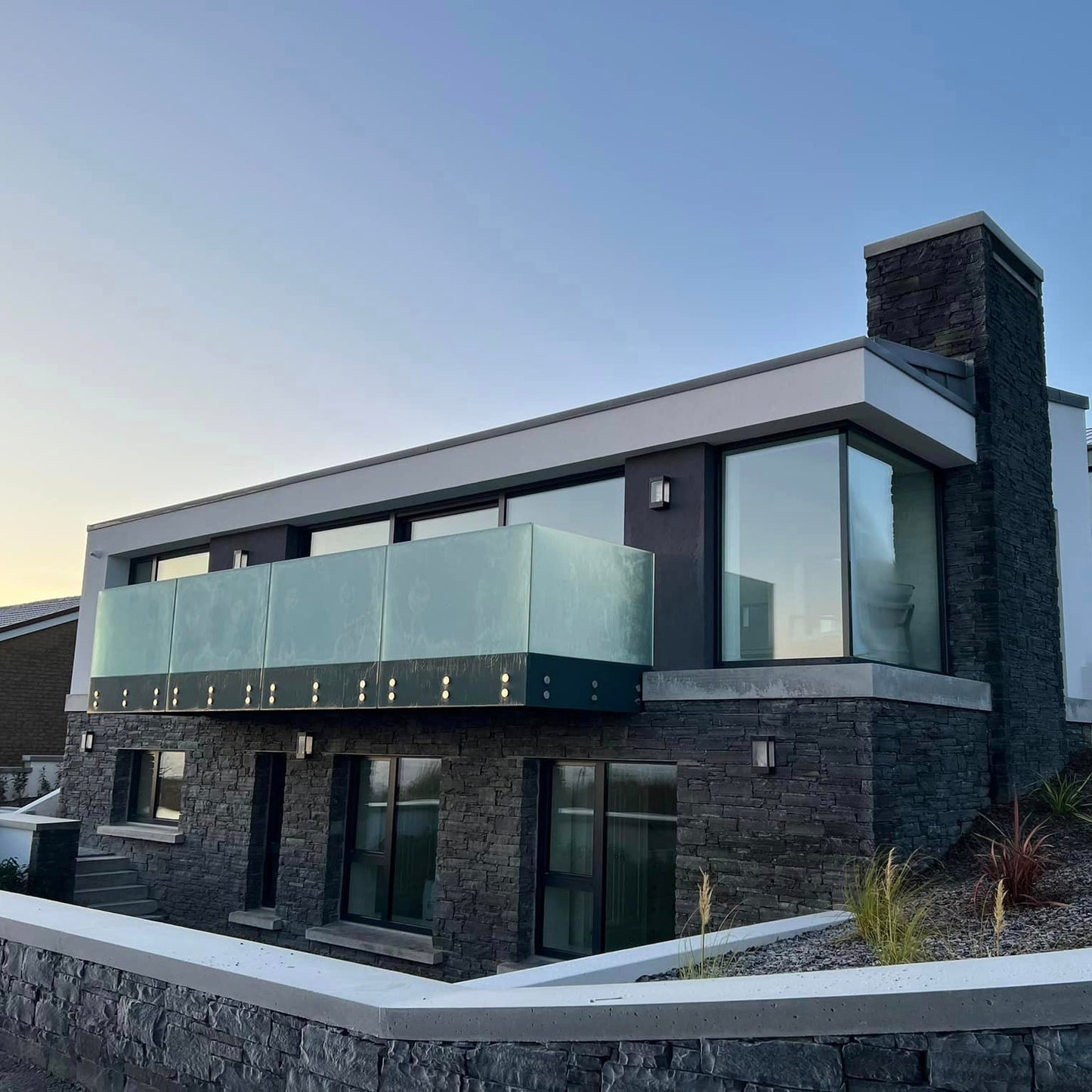 Modern stone clad house with glass balustrade on a clear day. Stonework is Liscannor Slate Stoneer Cladding. 