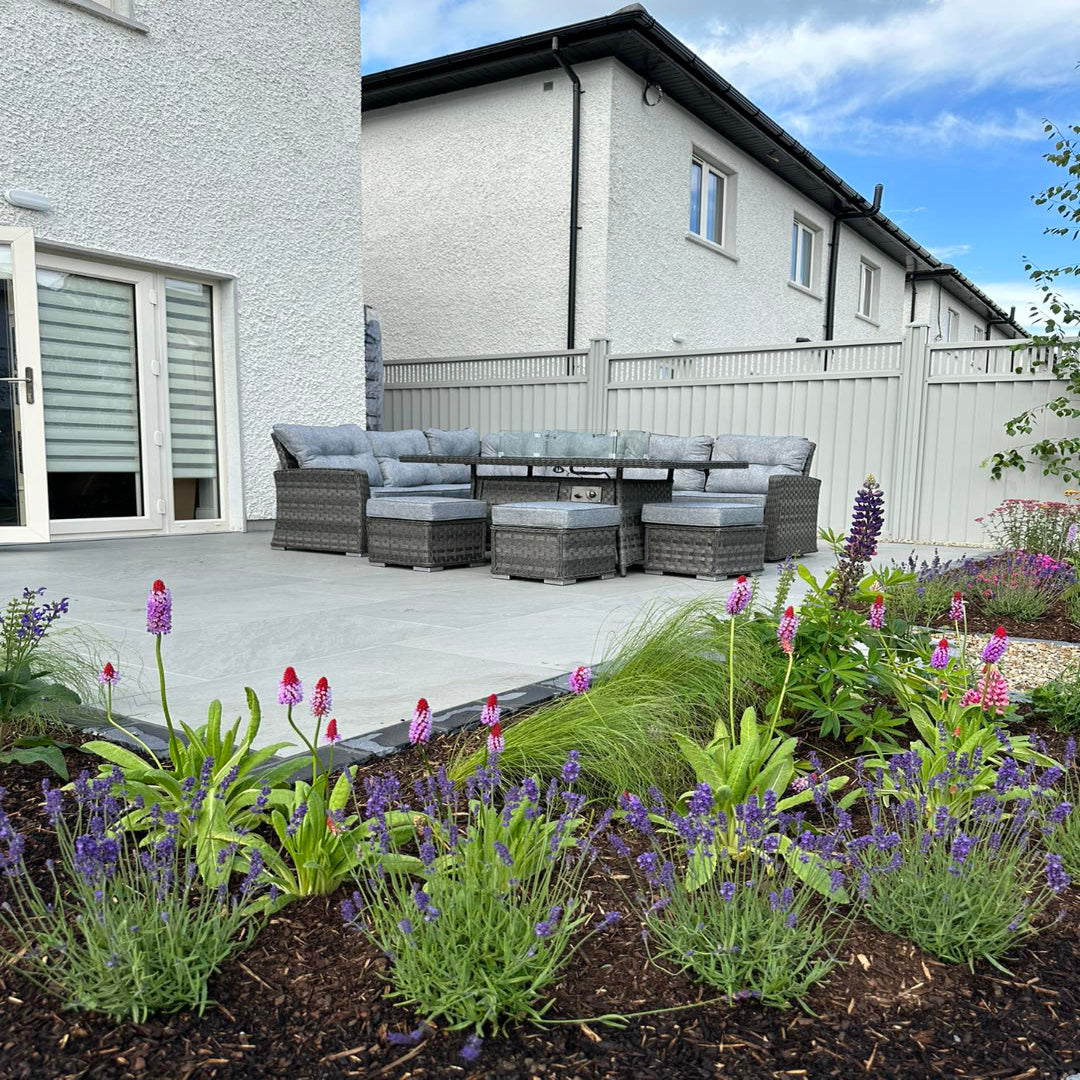 An outdoor setting featuring Mercury Grey porcelain paving with a garden and a seating area in the background.