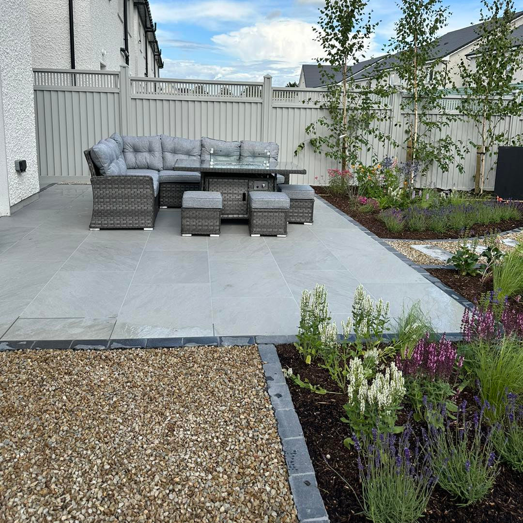 Patio area with garden furniture surrounded by planting and pathways completed using Mercury Grey Jewel Range Porcelain Paving. 