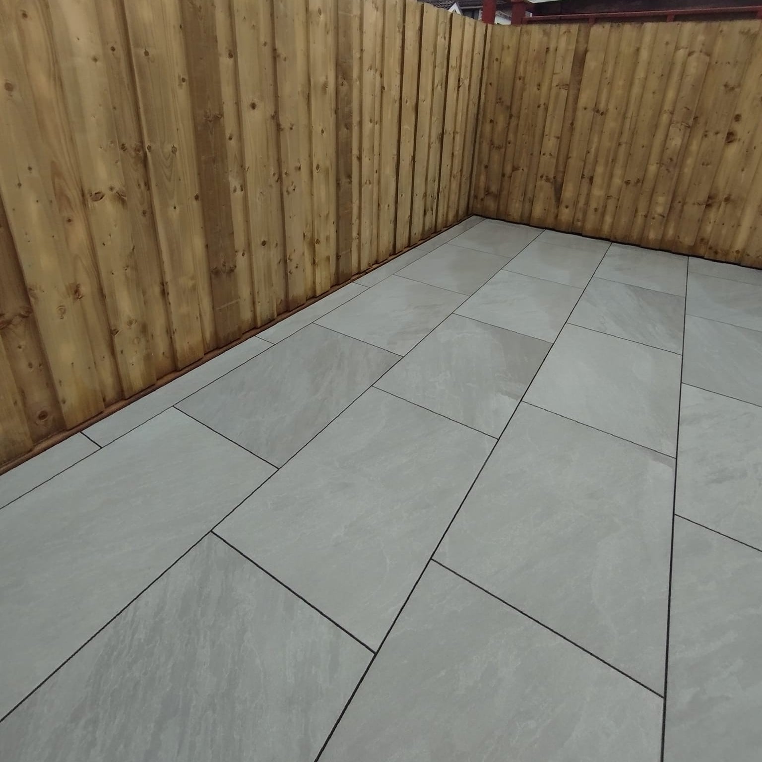 Patio area surrounded by a tall wooden fence. Paving is Mercury Grey Jewel Range Porcelain Paving. 