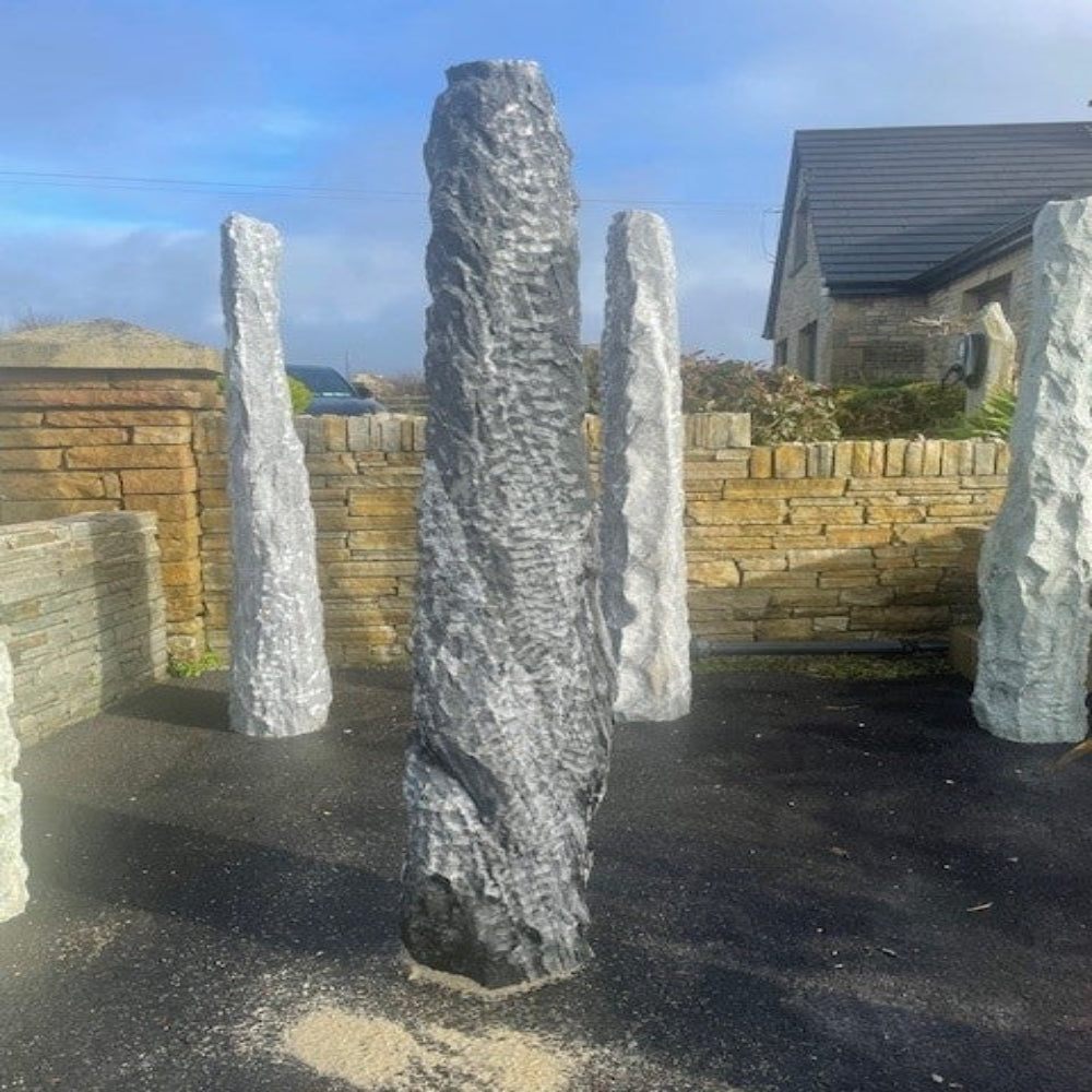 Large granite monolith called Mountain Wave in a outdoor setting with a house and wall in the background.