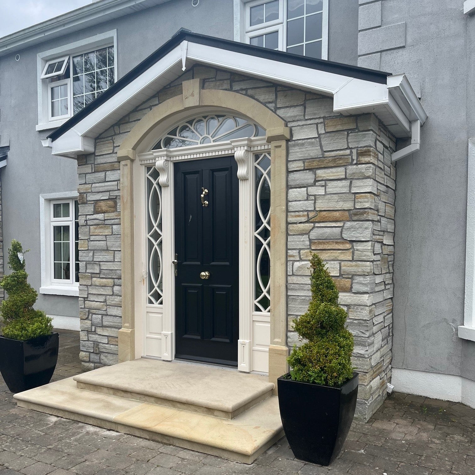 House with stone porch with a black door and decorative sandstone surround and steps. 