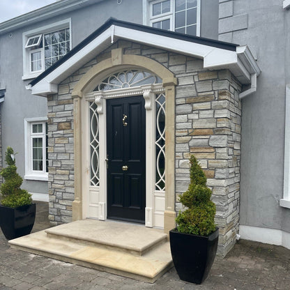 House with stone porch with a black door and decorative sandstone surround and steps. 