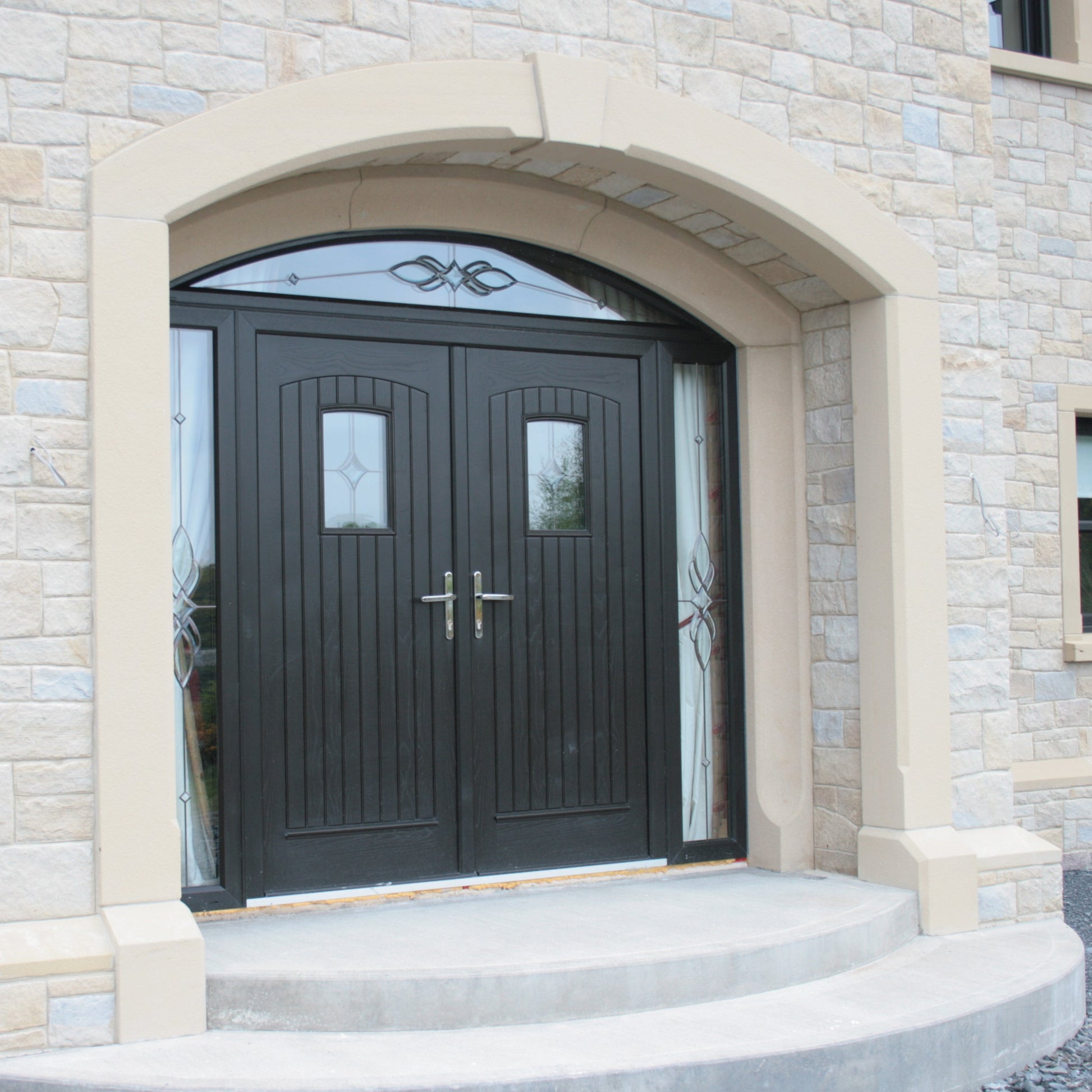 Bespoke sandstone door surround with double black doors and curved entrance steps. 