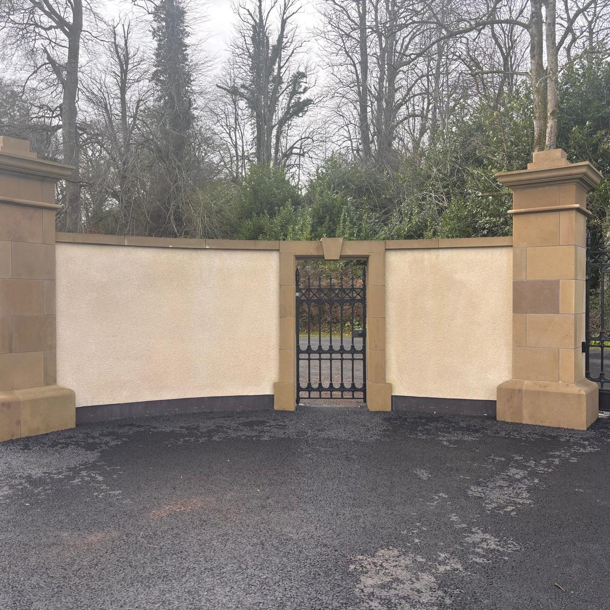 Boundary wall with bespoke sandstone door surround with black metal gate. 