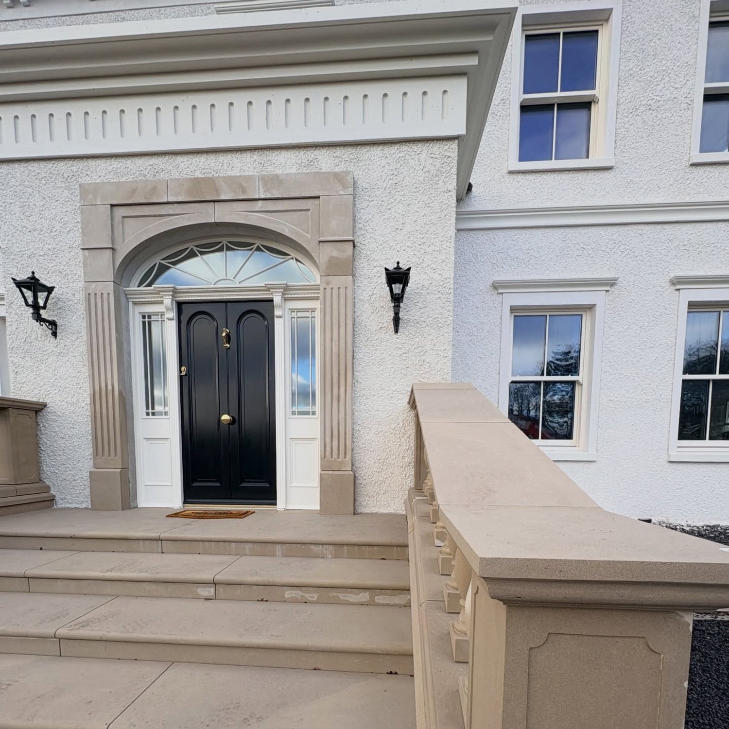 Front entrance of a large house with a black door, bespoke sandstone door surround and stone steps.