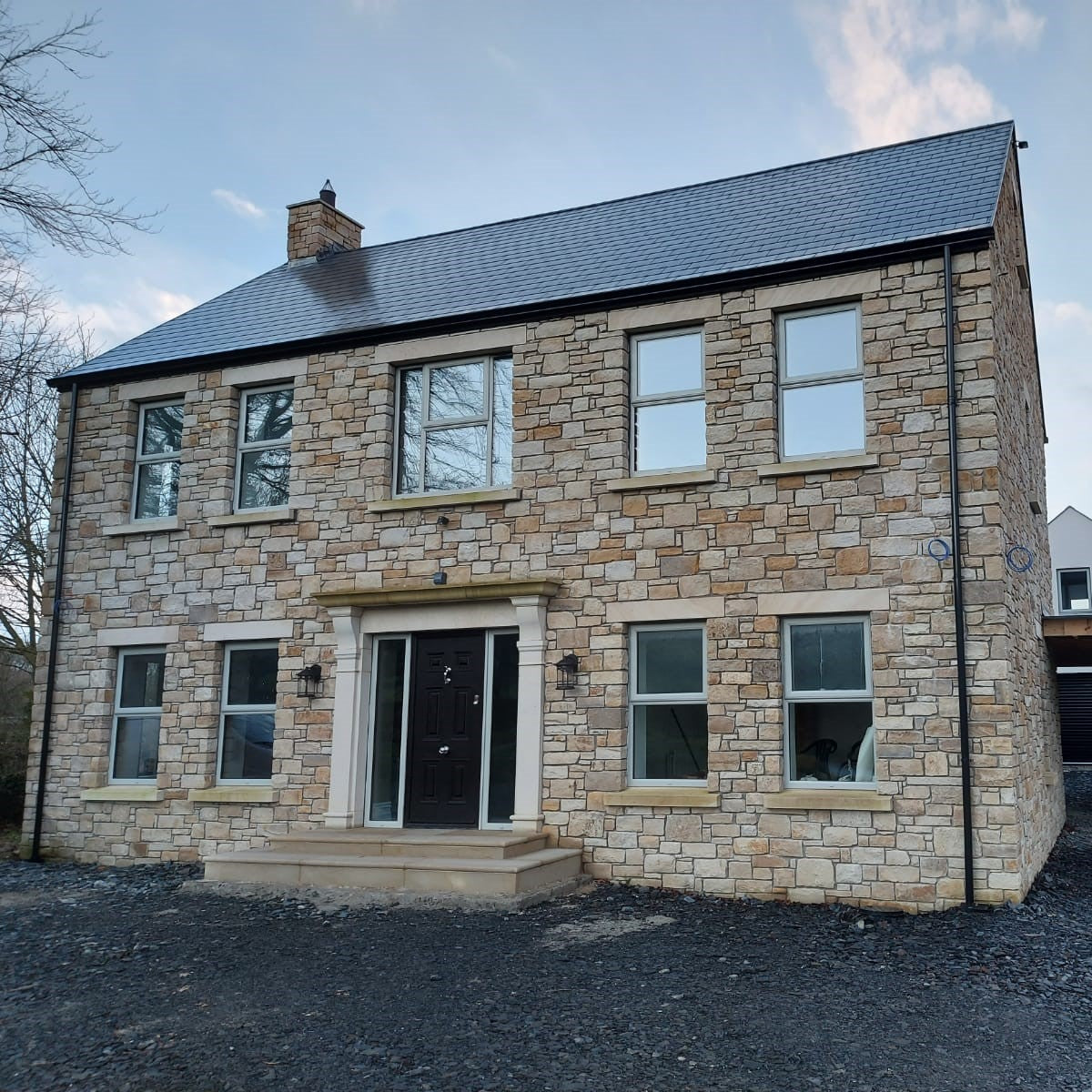 Two-story stone house with a car in the driveway on a clear day. Stone is Mountcharles Sandstone Machined.