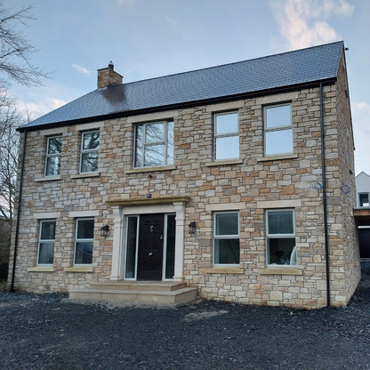 Two-story stone house with a car in the driveway on a clear day. Stone is Mountcharles Sandstone Machined.