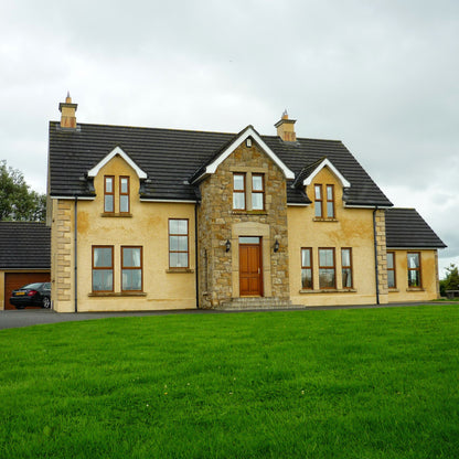 Large house with beige exterior and dark roof on a grassy lawn. Stone is Mountcharles Sandstone Machined.