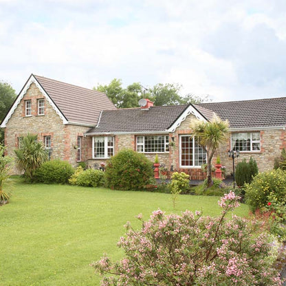 Stone house with a garden and trees on a clear day. Stone is Mountcharles Sandstone Machined Rubble. 