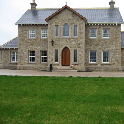 Large stone house with a wooden door and multiple windows on a clear day. Stone is Mountcharles Sandstone Machined Rubble. 