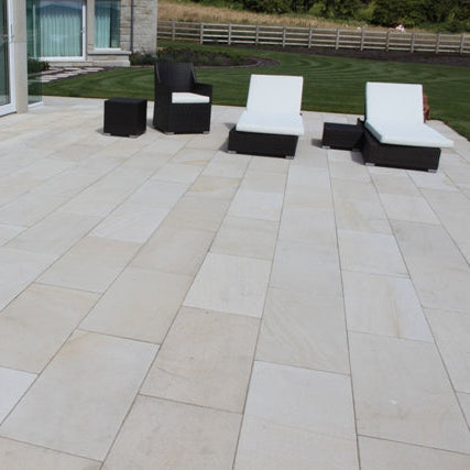 Mountcharles Sandstone Patio Slabs with sun lounger garden furniture and well maintained garden in the background. 