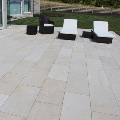 Mountcharles Sandstone Patio Slabs with sun lounger garden furniture and well maintained garden in the background. 