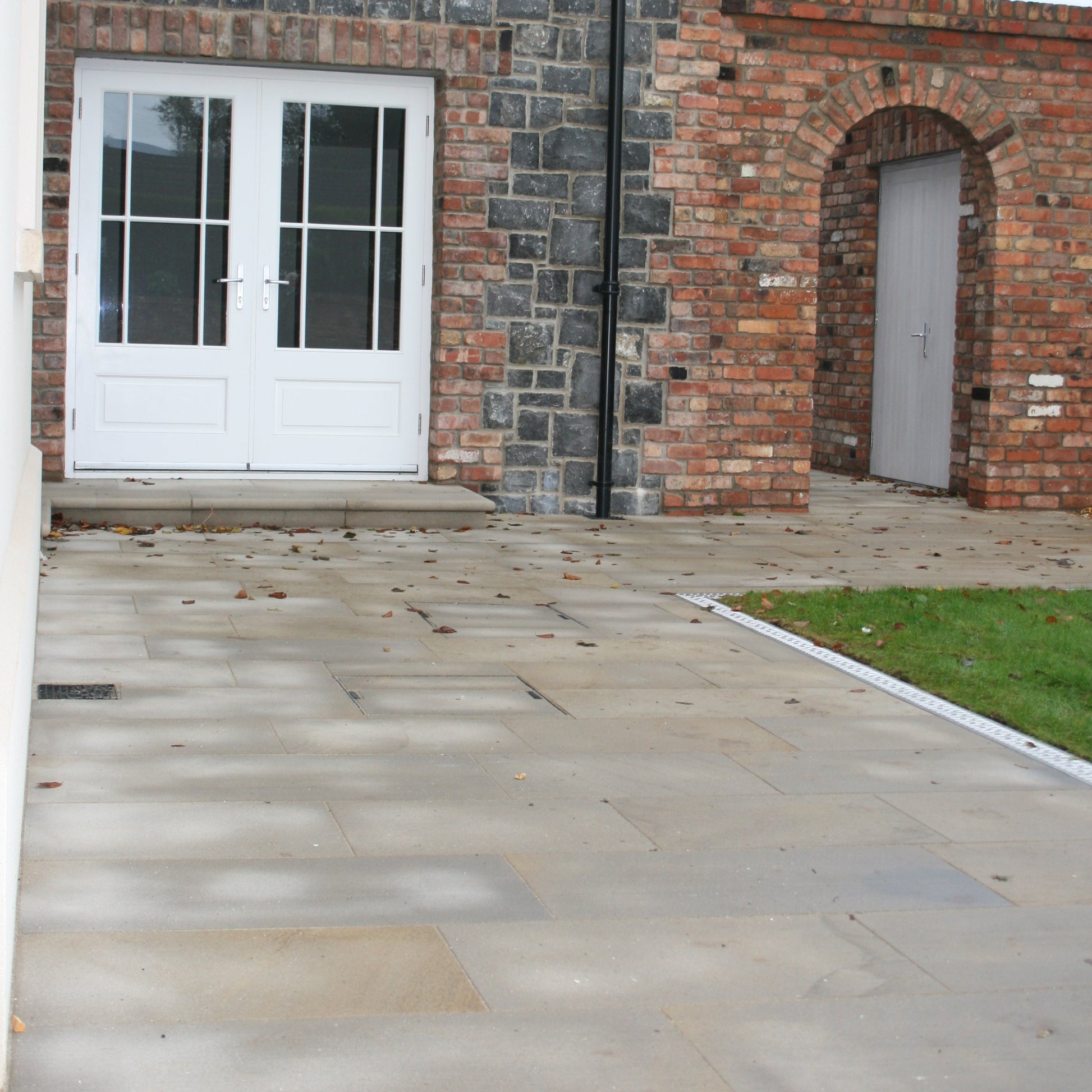 Mountcharles Sandstone paving installed to a pathway leading to white double doors and Mountcharles Sandstone step.
