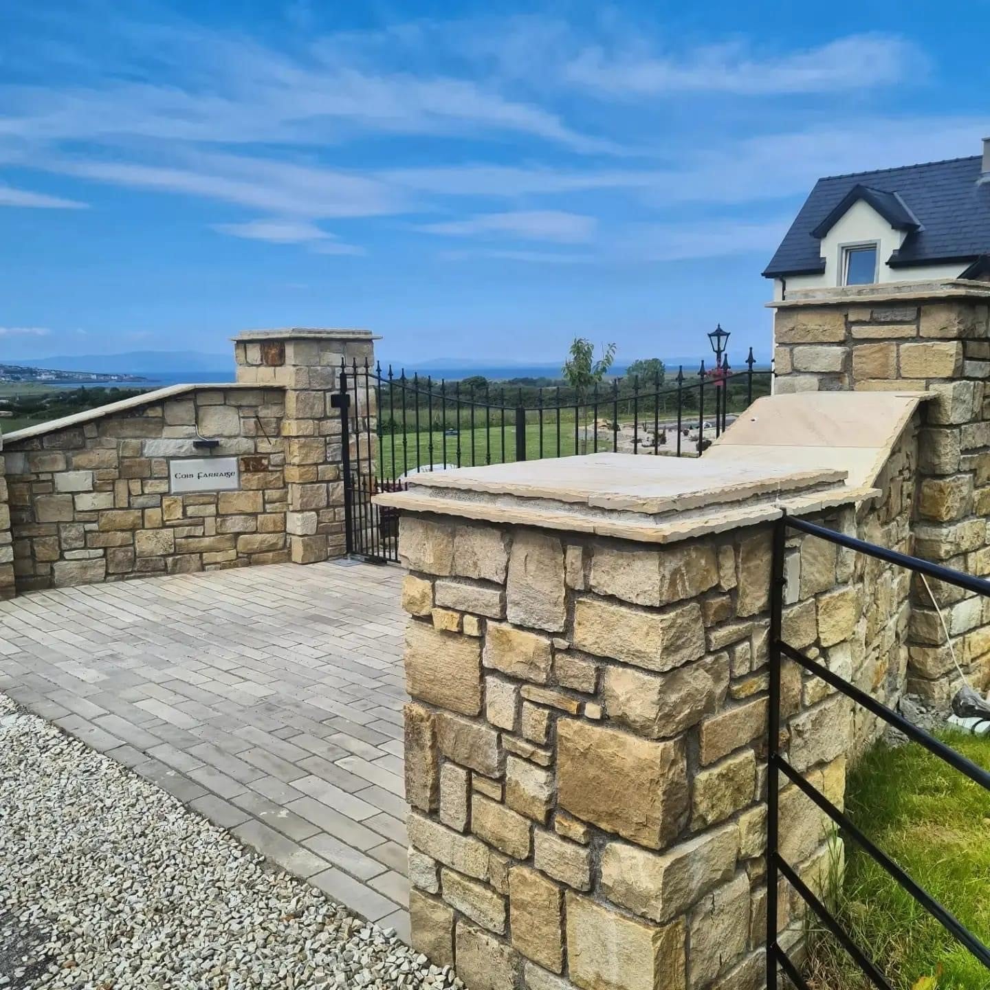 Driveway entrance with stone wall and black gate completed using Mountcharles Sandstone Paving Setts in Random Length x 100mm.