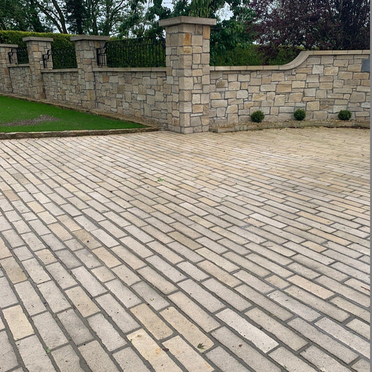 Driveway paved using Mountcharles Sandstone Paving Setts in Random Length x 100mm. Stone boundary wall and grass in the background. 