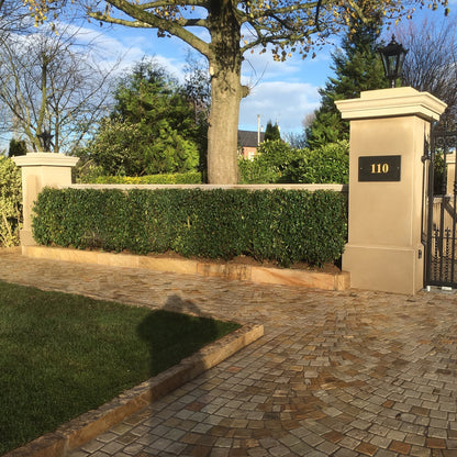 Bespoke Sandstone Pillar Capping and Wall Capping on entrance walls with a black gate and trees in the background. 