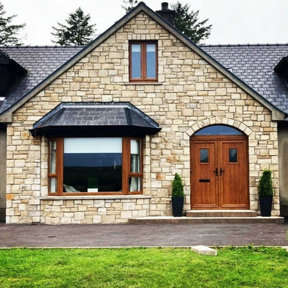 Stone wall façade with brown door and windows. Stonework is Mountcharles Sandstone Stoneer Cladding. 