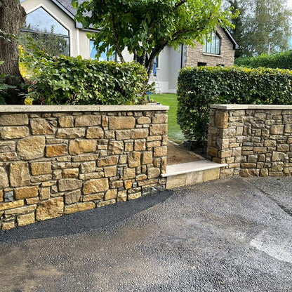 Stone wall with a driveway leading to a house. Stone is Mountcharles Sandstone Tumbled. 