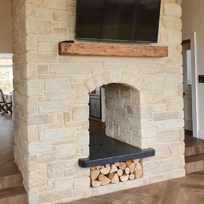 Stone fireplace with a TV mounted above it and firewood below. Stone is Mountcharles Sandstone tumbled walling stone. 