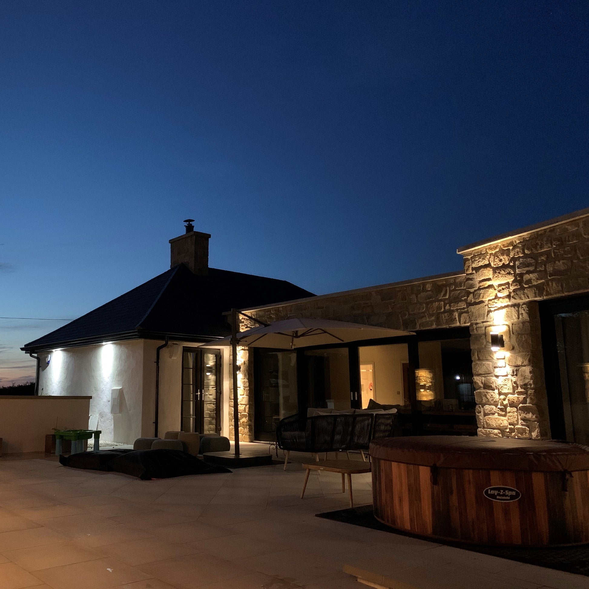 Evening view of a modern house with outdoor lighting and furniture. Stonework is Mountcharles Sandstone tumbled walling stone.