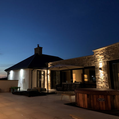 Evening view of a modern house with outdoor lighting and furniture. Stonework is Mountcharles Sandstone tumbled walling stone.