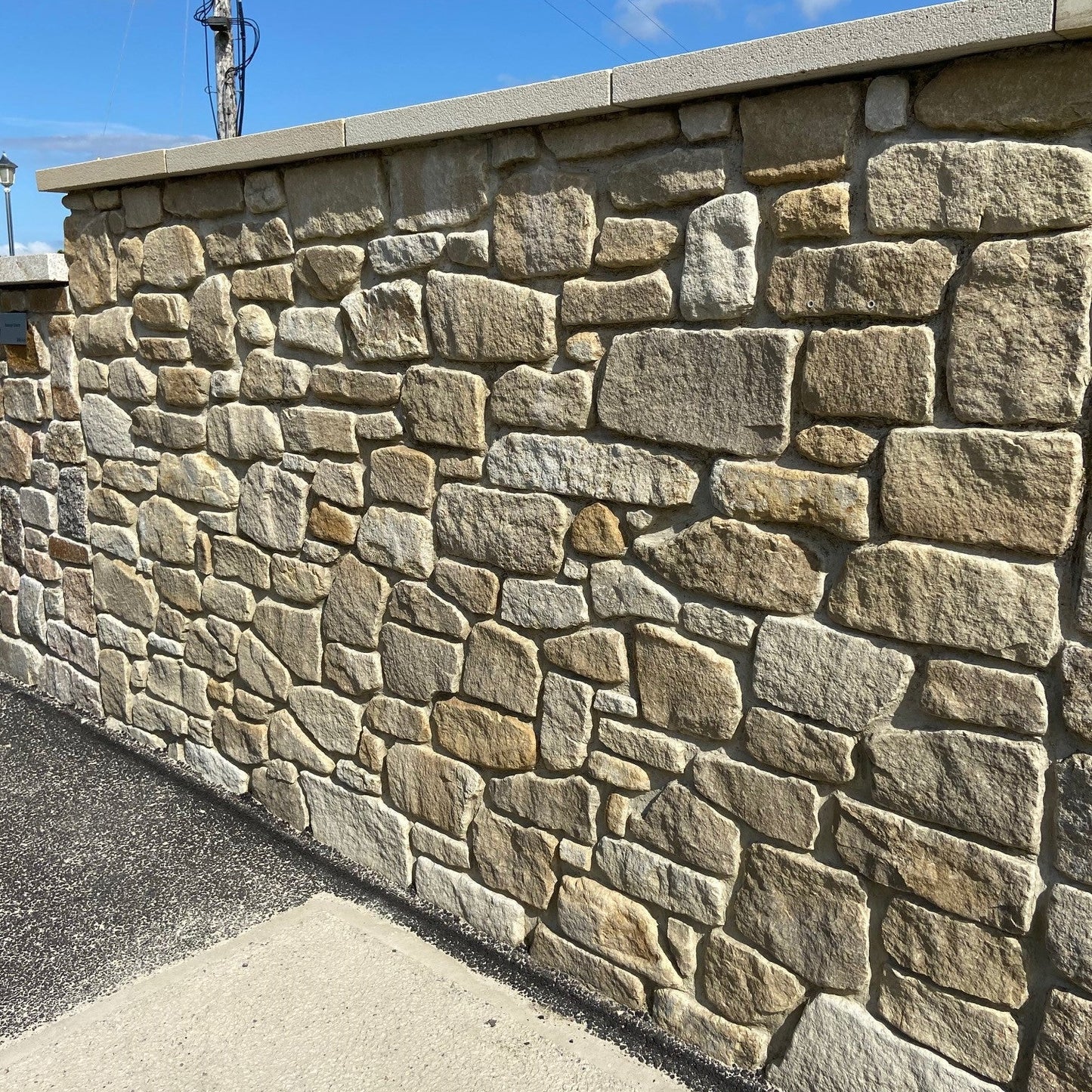 Stone wall finished in Mountcharles Sandstone Tumbled walling stone with a blue sky and power line in the background