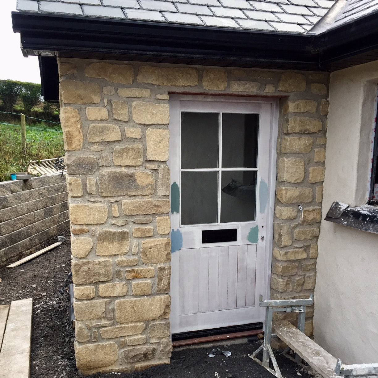 Stone exterior wall completed in Mountcharles Sandstone Tumbled with a white door and window of a house under construction.