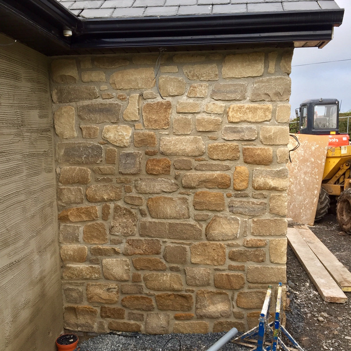 Stone wall of a building under construction with tools and materials around. Stonework is Mountcharles Sandstone - Tumbled. 