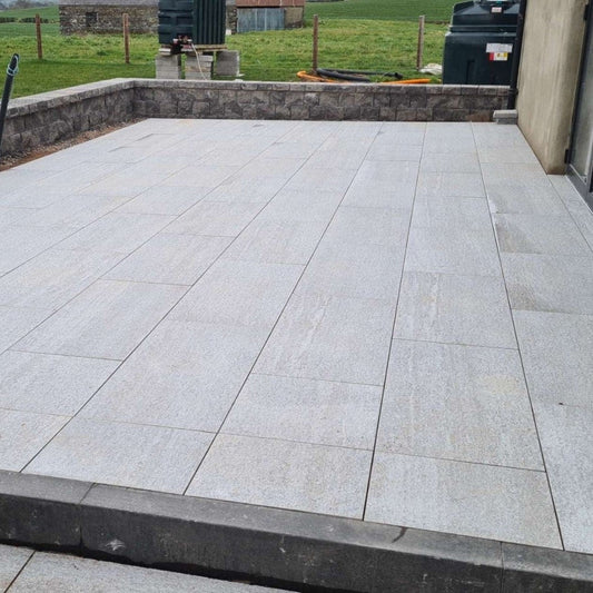 An outdoor installation of Pietra di Bagnolo porcelain tiles in a garden setting, showcasing their dark grey colour and rectangular shape.