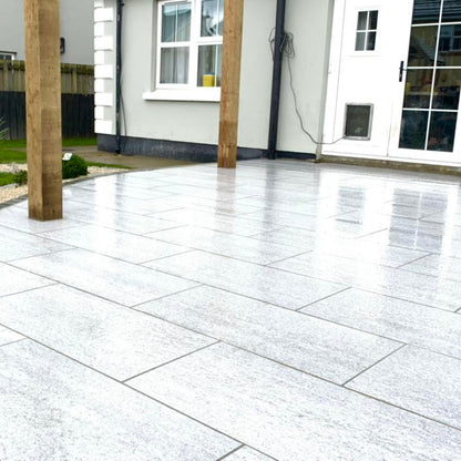 Paved patio area in a garden with a house in the background. Paving is Pietra di Bagnolo porcelain tiles. 