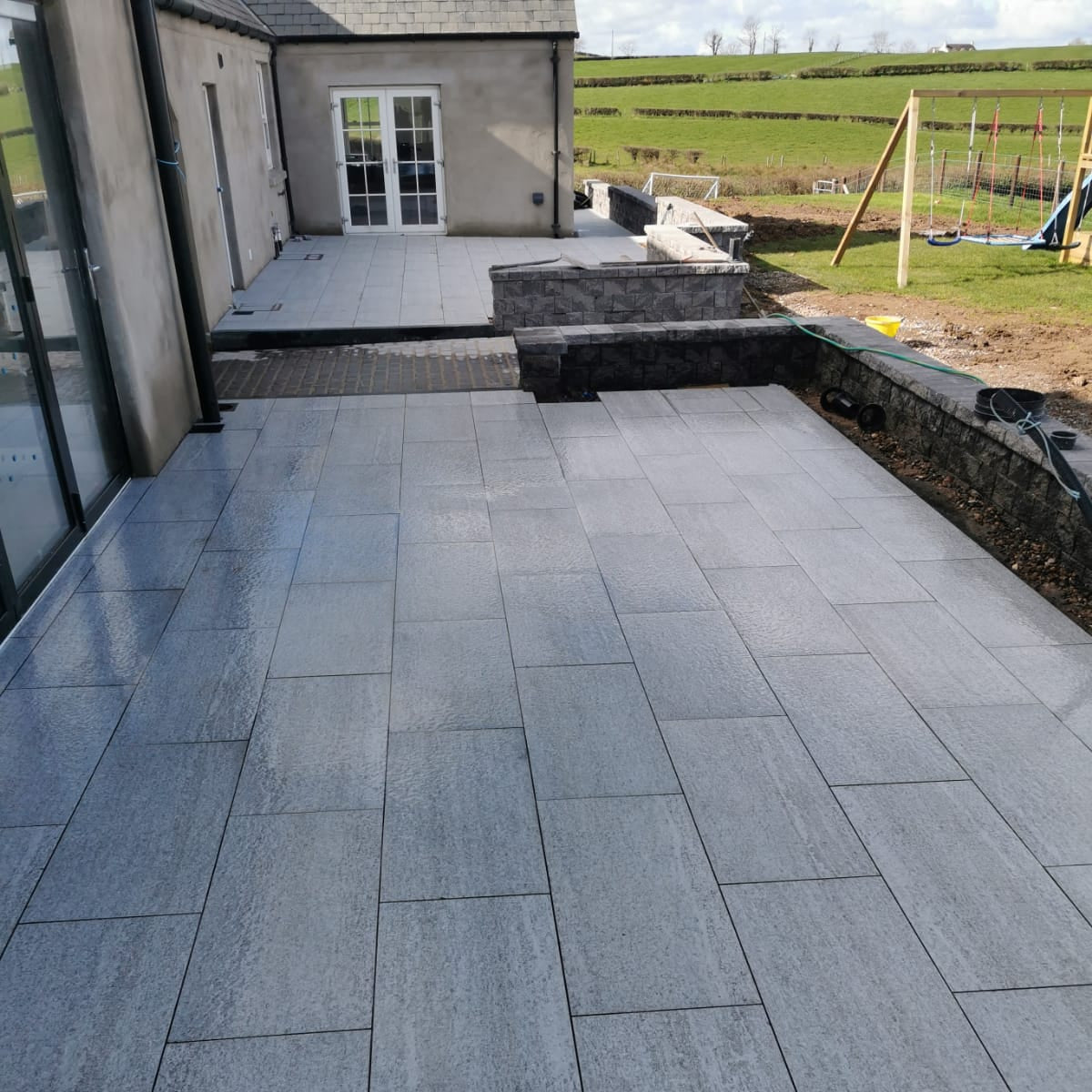 An outdoor patio showcasing Pietra di Bagnolo porcelain tiles in a garden setting.